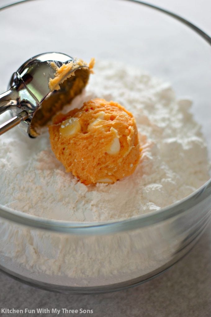scooping the orange dough into a clear bowl filled with powdered sugar